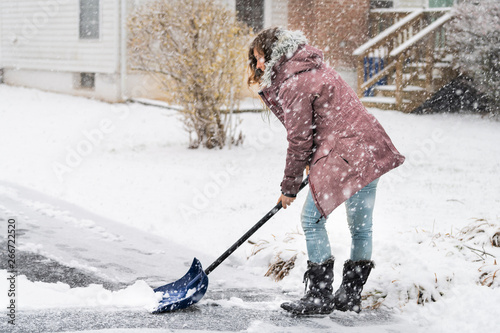 Wall Mural Young woman in winter coat cleaning shoveling driveway street from snow in heavy