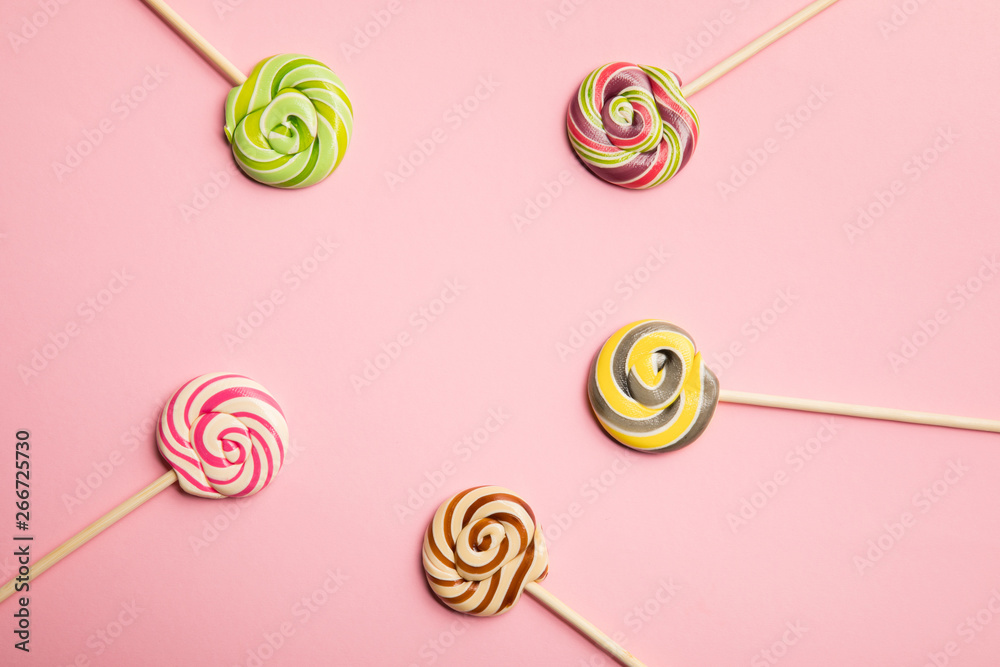 top view of delicious multicolored swirl lollipops on wooden sticks on pink background