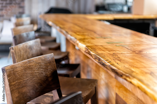 Row of empty wooden vintage bar stools by counter in drink establishment pub during day closeup of retro wood and nobody
