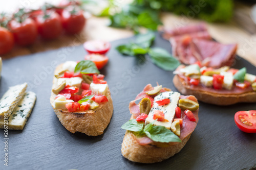 Traditional Italian bruschetta with blue cheese, feta, tomatoes, basil leaves, jamon on black stone background. © Konstiantyn Zapylaie