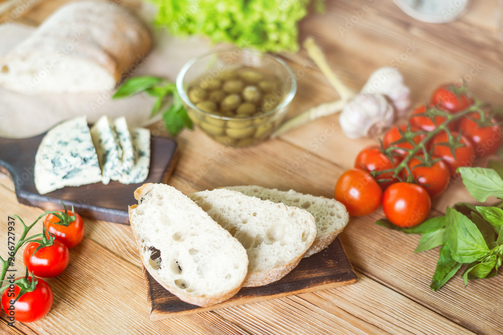 Ingredients for cooking bruschetta: chopped ciabatta, olives, tomatoes, blue cheese on a wooden background. Cooking healthy and tasty food. Ingredients for cooking bruschetta: chopped ciabatta, olives, tomatoes, blue cheese on a wooden background. Cooking healthy and tasty food.