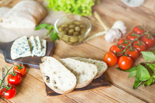 Ingredients for cooking bruschetta: chopped ciabatta, olives, tomatoes, blue cheese on a wooden background. Cooking healthy and tasty food.