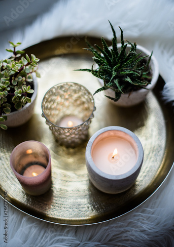 Cozy real home decoration, burning candles on golden tray with pillow on white faux fur on windowsill