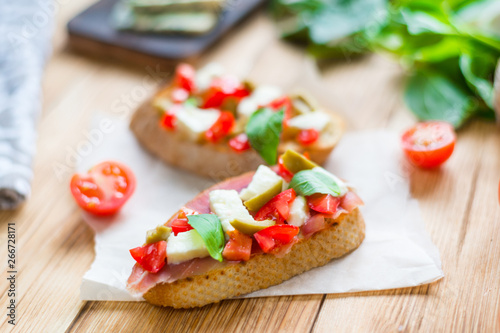 Traditional Italian bruschetta with blue cheese, feta, tomatoes, basil leaves, jamon on a wooden background.