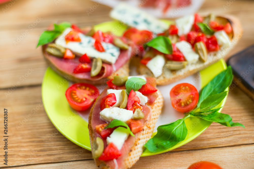 Traditional Italian bruschetta with blue cheese, feta, tomatoes, basil leaves, jamon on a wooden background. Traditional Italian bruschetta with blue cheese, feta, tomatoes, basil leaves, jamon on a wooden background.