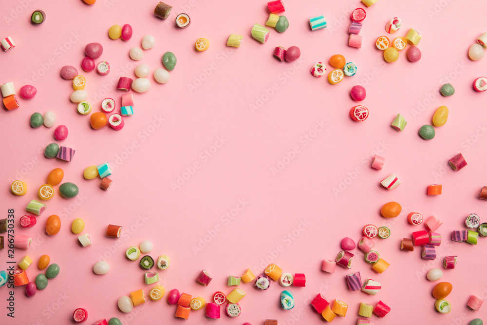 top view of multicolored candies scattered on pink background with copy space