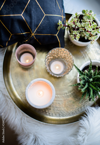 Cozy real home decoration, burning candles on golden tray with pillow on white faux fur on windowsill