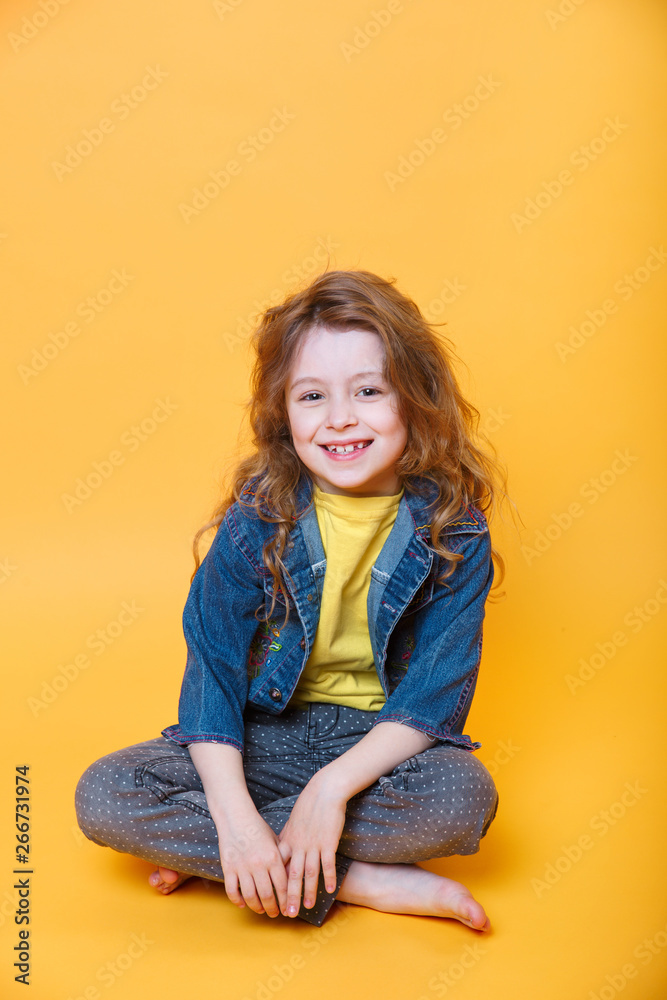 Cute little girl sitting with crossed legs on orange background Cute little girl sitting with crossed legs on orange background