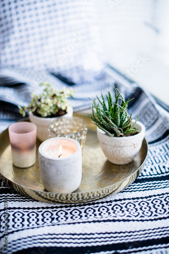 Real apartment interior decor  aromatic candles and plants on vintage tray with pillows and blanket on white windowsill