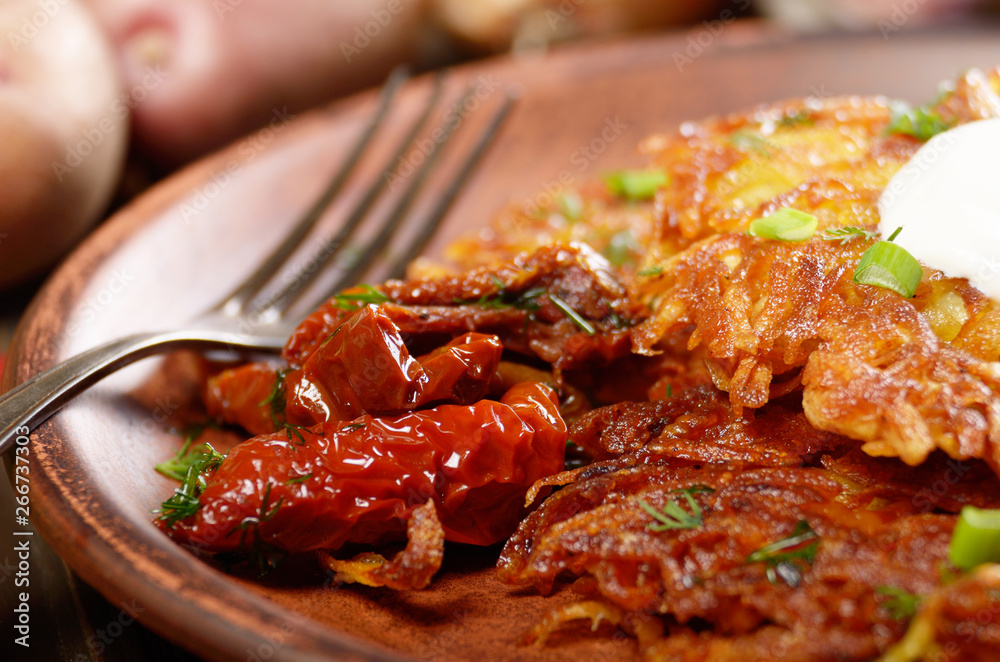 Closeup view at Homemade tasty potato pancakes in clay dish with sun-dried tomatoes and sour creram Closeup view at Homemade tasty potato pancakes in clay dish with sun-dried tomatoes and sour creram