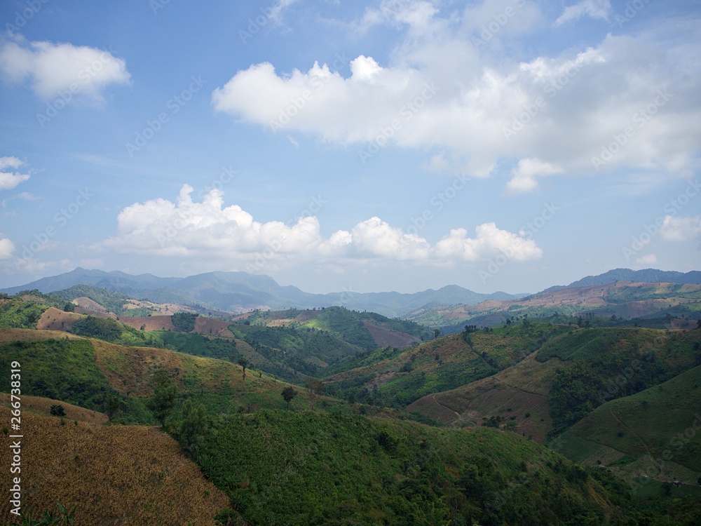 Landscape shot of the green mountain valley, dried corn field and the blue sky with cloud, Nan, Thailand