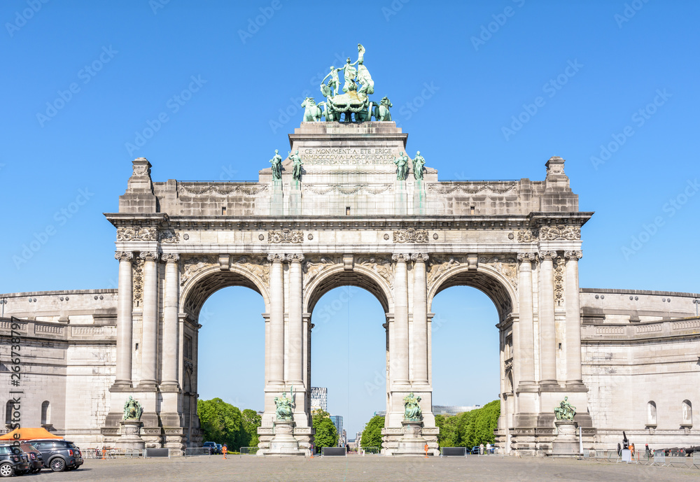 Front view of the eastern side of the arcade du Cinquantenaire, the triumphal arch erected in 1905 by king Leopold II in the Cinquantenaire park in Brussels, Belgium, against blue sky.