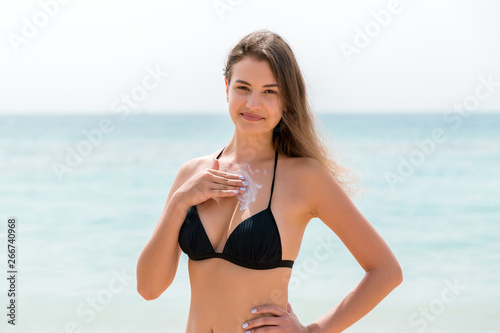 Attractive woman is applying sunblock on her breast with the fingers at the sea background
