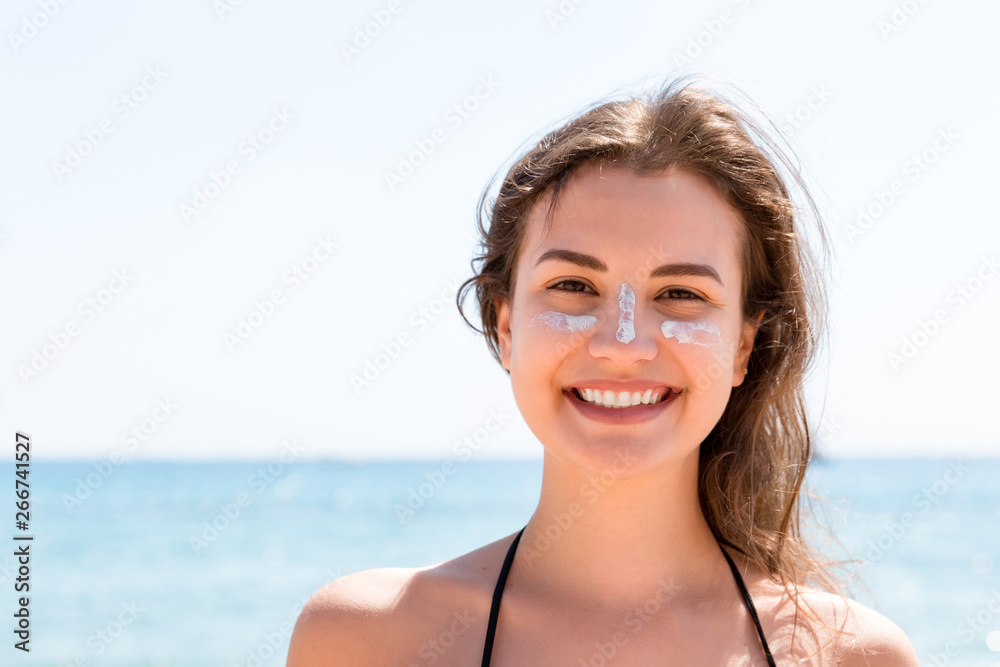 Beautiful young woman is posing at the camera with suncream on her face over the sea background Beautiful young woman is posing at the camera with suncream on her face over the sea background