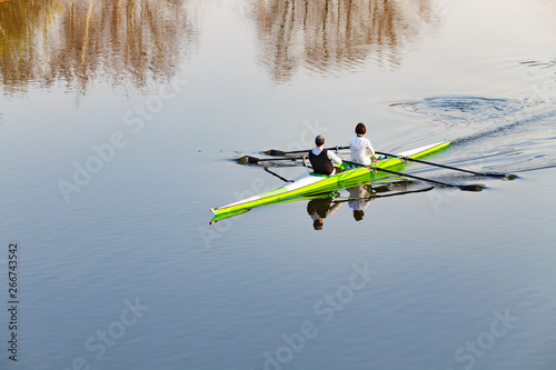 Man and woman rowing in yellow double scull boat. Calm water surface as background with copy space