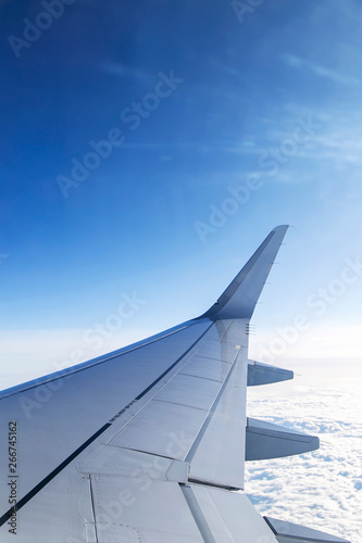 Window view of aircraft wing flying over clouds in blue sky