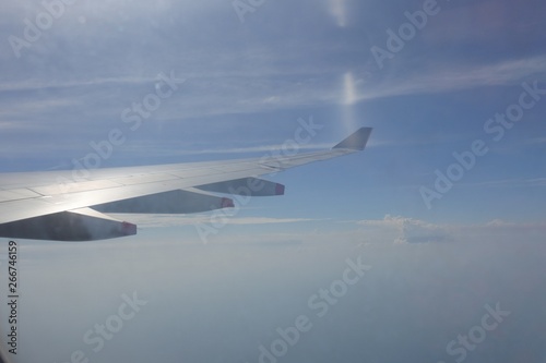 Airplane wing out of window with blue sky and white cloud background
