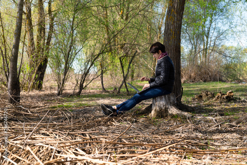 Girl using lap top among nature. Time online. Is sits on a stump near a tree © Iakov