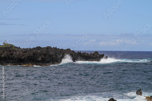 Wellen an vulkanischer Felsenküste mit blauen Himmel und Wolken
