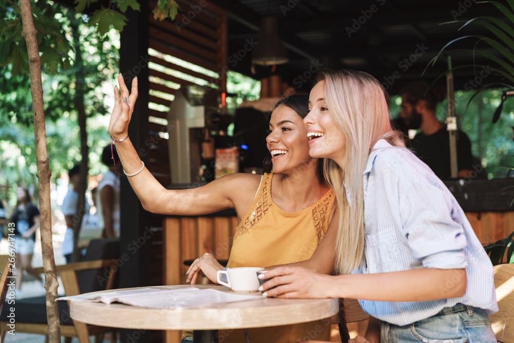 Two cheerful young girlfriends sitting at the cafe table Two cheerful young girlfriends sitting at the cafe table