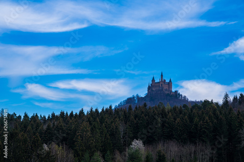 Germany, Hohenzollern castle on a hill behind green conifer edge of the forest