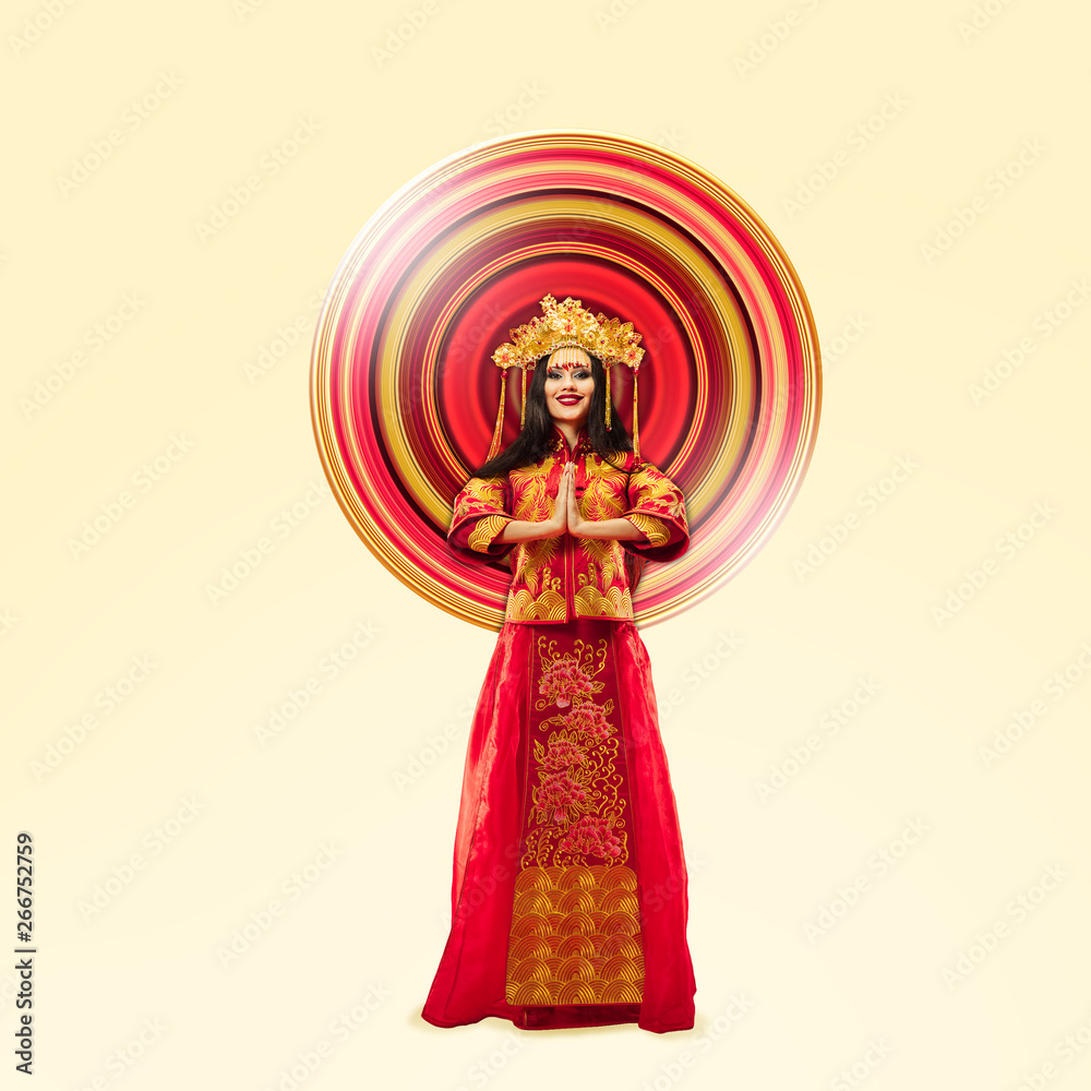 Woman standing in red and gold traditional costume isolated on yellow studio background. Negative space. Beauty, movement, action and moving, advertising concept. Abstract design.