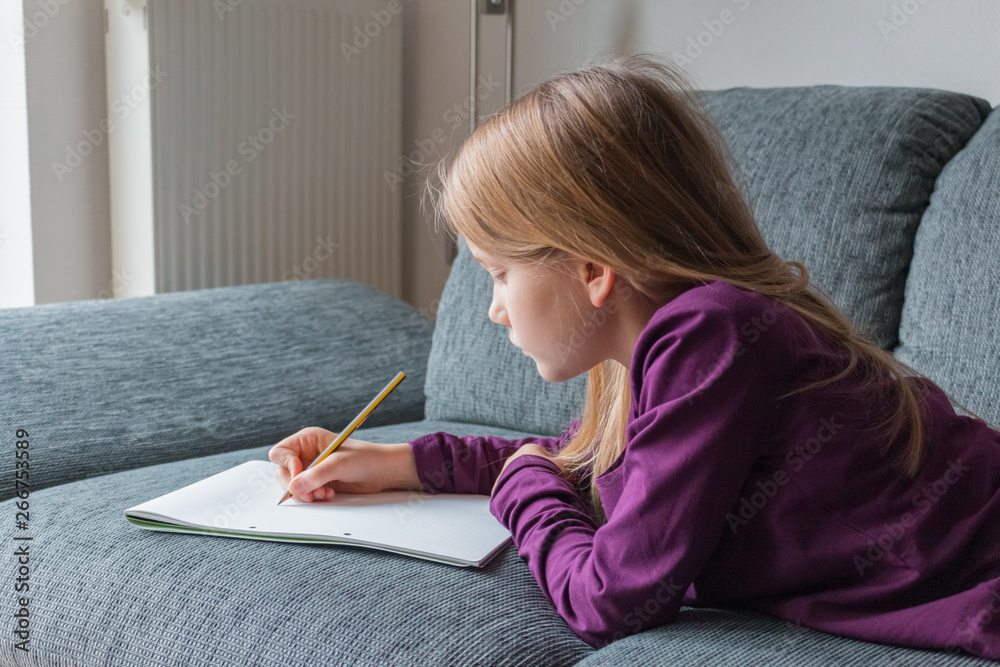 A girl is lying on a couch and is writing with a pencil on paper notes A girl is lying on a couch and is writing with a pencil on paper notes
