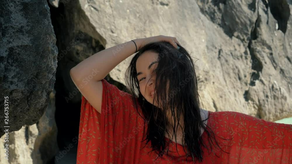 Young pretty girl wearing red dress standing between the rocks and looking into the camera. Attractive model posing between rocks. Young pretty girl wearing red dress standing between the rocks and looking into the camera. Attractive model posing between rocks.
