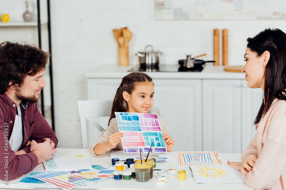 Fototapeta premium cheerful kid holding paper with colorful stripes near parents at home