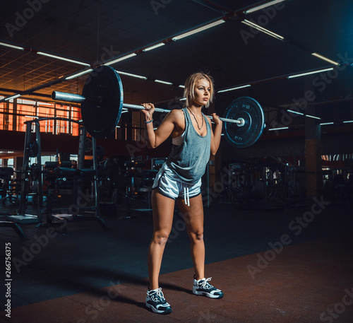 Fototapeta Naklejka Na Ścianę i Meble -  Strong Athletic Woman in Sportswear Lifts Heavy Barbell and Does Squats with it as a Part of Her Fitness. classic bodybuilding. hardcore doing exercise by fitness girl
