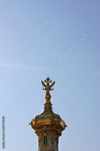 Golden dome with two headed eagle - symbol of russian empire on top. Gilded cupola close up view isolated on blue sky background 
