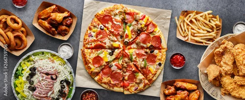 Obraz large table of assorted take out food such as pizza, french fries, onion rings, fried chicken and chicken wings