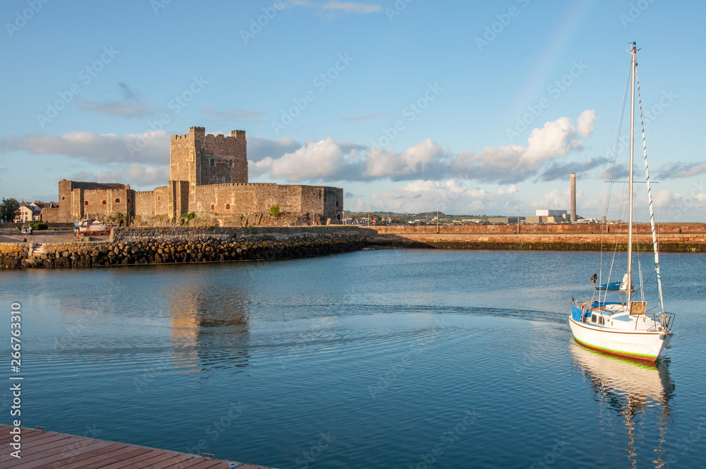 Medieval Norman Castle, yacht, harbor, breakwater and power plant in Carrickfergus near Belfast, Northern Ireland, UK, in sunset light