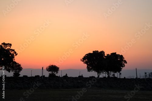 Stunning sunrise view at the Sea of Galilee with silhouette of trees and tourists