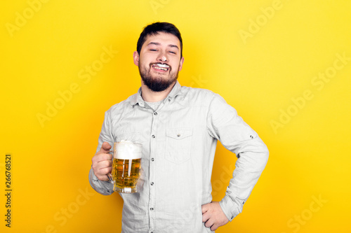 funny man with a glass of beer and foam on his mustache and nose over yellow background, party concept © alesmunt