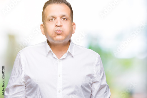 Middle age arab elegant man over isolated background puffing cheeks with funny face. Mouth inflated with air, crazy expression.