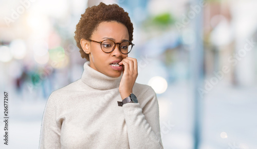 Young beautiful african american woman wearing glasses over isolated background looking stressed and nervous with hands on mouth biting nails. Anxiety problem.