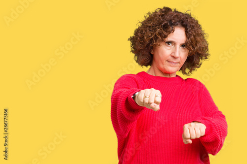 Beautiful middle ager senior woman red winter sweater over isolated background Punching fist to fight, aggressive and angry attack, threat and violence