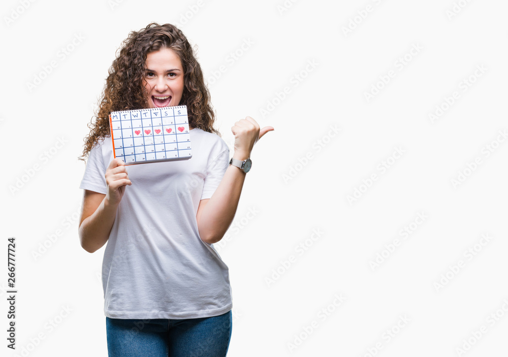 Young brunette girl holding menstruation calendar over isolated background pointing and showing with thumb up to the side with happy face smiling Young brunette girl holding menstruation calendar over isolated background pointing and showing with thumb up to the side with happy face smiling