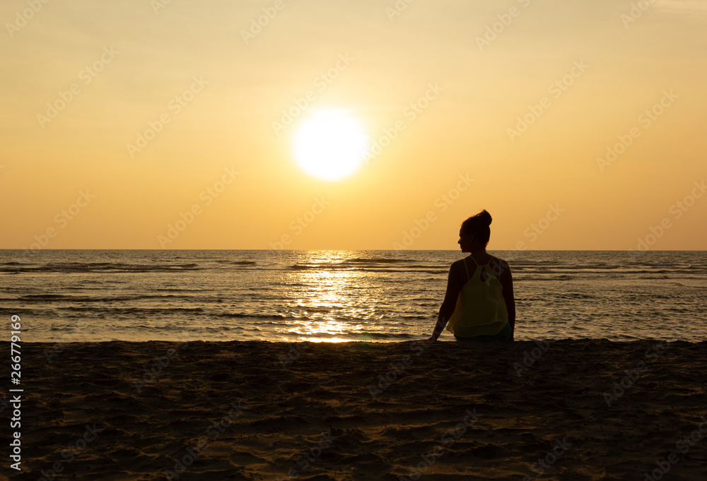 Silhouette of a young woman against the backdrop of the sunset and the big sun