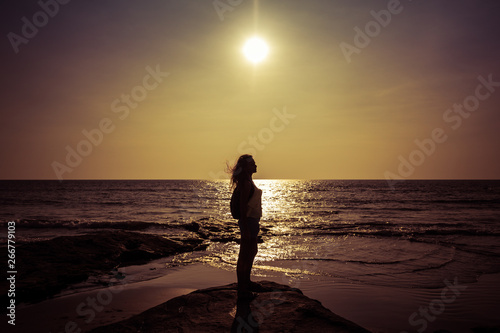 Silhouette of a young woman against the background of the sea and the sun