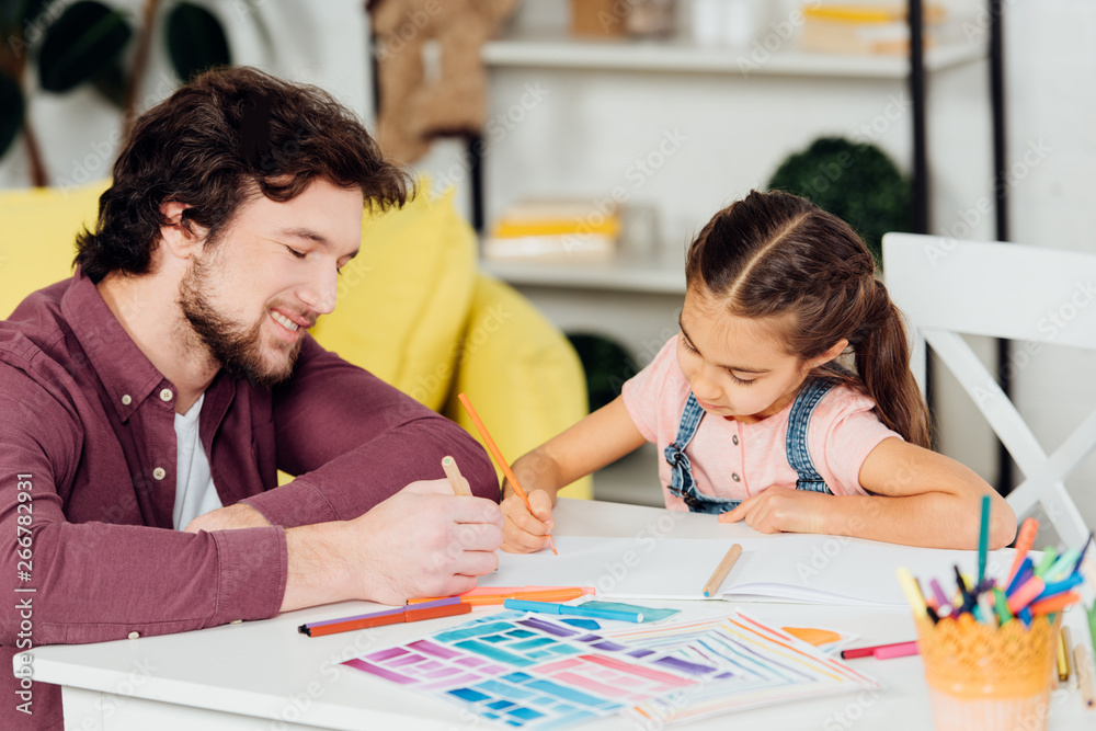 cheerful father drawing on paper near cute daughter at home cheerful father drawing on paper near cute daughter at home