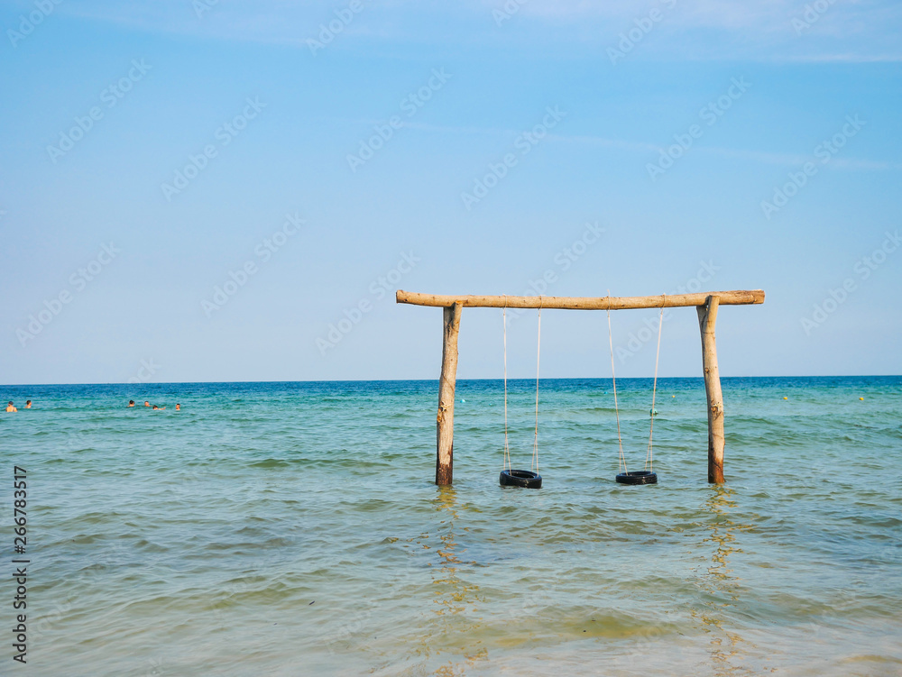 Beautiful sea landscape. High wooden swing decorated with colorful ribbons in a calm azure sea near the coastline. Beautiful sea landscape. High wooden swing decorated with colorful ribbons in a calm azure sea near the coastline.
