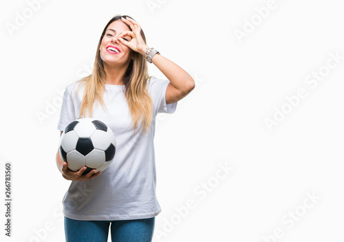 Young beautiful woman holding soccer ball over isolated background with happy face smiling doing ok sign with hand on eye looking through fingers