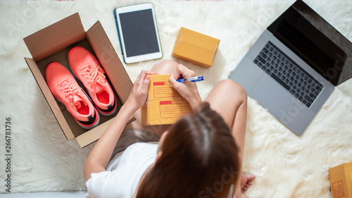 Woman entrepreneur owner SME business is checking order with smartphone, laptop and packaging box to send her client