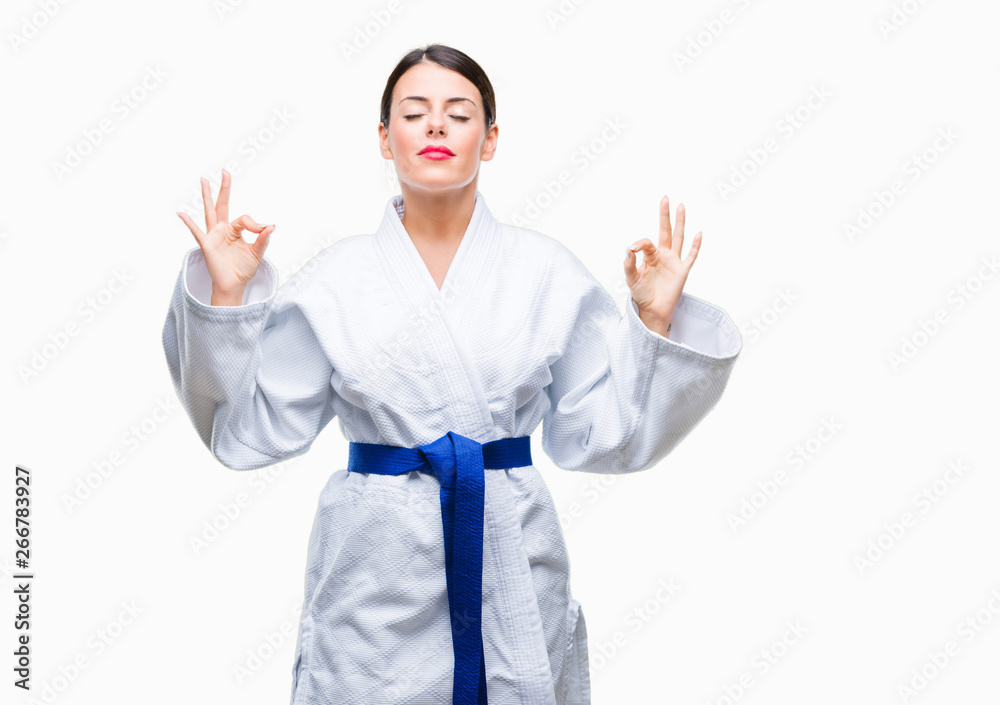 Young beautiful woman wearing karate kimono uniform over isolated background relax and smiling with eyes closed doing meditation gesture with fingers. Yoga concept. Young beautiful woman wearing karate kimono uniform over isolated background relax and smiling with eyes closed doing meditation gesture with fingers. Yoga concept.