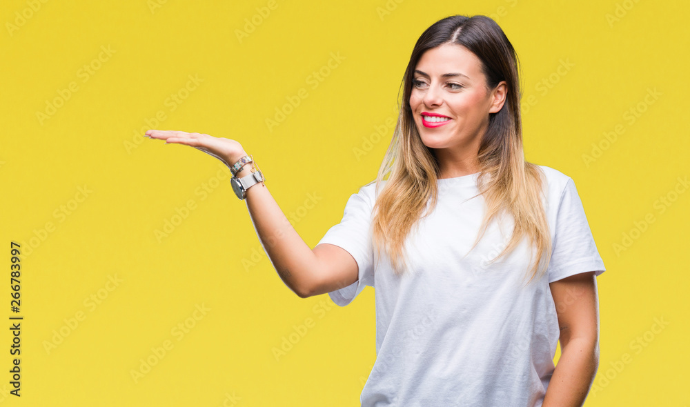 Young beautiful woman casual white t-shirt over isolated background smiling cheerful presenting and pointing with palm of hand looking at the camera. Young beautiful woman casual white t-shirt over isolated background smiling cheerful presenting and pointing with palm of hand looking at the camera.