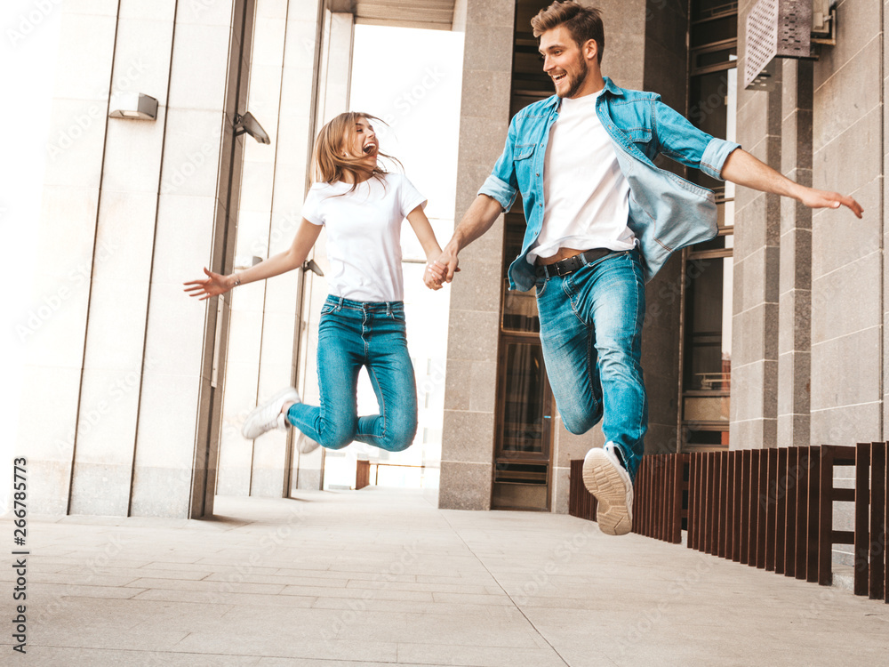 Portrait of smiling beautiful girl and her handsome boyfriend in casual summer clothes. Happy cheerful family jumping and having fun on the street background. Going crazy