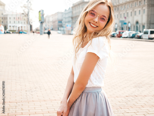 Portrait of beautiful smiling blond model dressed in summer hipster  clothes. Trendy girl posing in the street background in round sunglasses. Funny and positive woman having fun