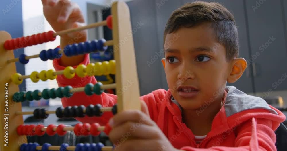 Front view of Asian schoolboy solving math problem with abacus at desk in a classroom at school 4k